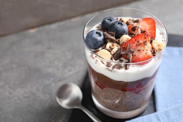 Delicious chocolate pudding with chia seeds, nuts and berries in glass on grey table, closeup....