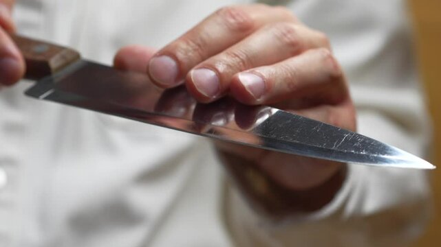 A sharp knife in the hands of a chef.
A man touches the sharp blade of his knife before using it.
A sharp knife made of steel.
A sharp steel knife