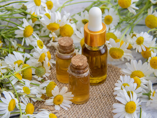 Bottles of essential oil and chamomile flowers on table, closeup