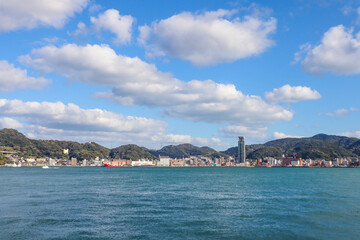 Fototapeta premium Panoramic View of Kitakyushu Skyline with Mountains and Ocean under Blue Sky, Japan