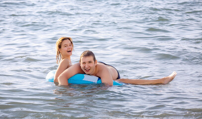 A cheerful young couple swims in the sea with an inflatable circle