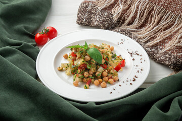 Warm composition with chickpea vegetable salad served on a white plate. Topped with fresh herbs,...