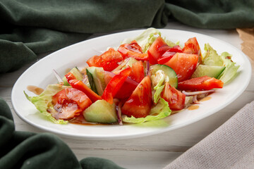 Colorful vegetable salad made of tomatoes, cucumbers, bell pepper, red onion and lettuce, served with balsamic dressing. Plated on a white dish with rustic background. Healthy and refreshing meal
