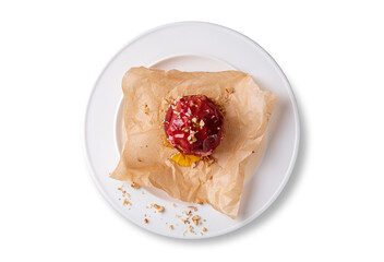 Top-down shot of a whole baked red apple glazed with honey and sprinkled with chopped walnuts. Served on crumpled parchment paper atop a clean white plate. Healthy homemade dessert perfect