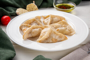 Close-up of homemade dumplings served on a white plate. Garlic, olive oil with spices, tomato, and green textile napkins create cozy kitchen atmosphere. Natural light food photography