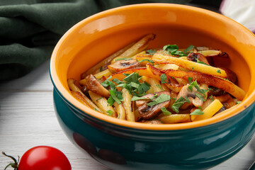 Close-up of golden fried potato strips with sautéed mushrooms and fresh chopped parsley, served in a deep orange and teal rustic ceramic bowl. A comforting, home-style dish on a light wooden table