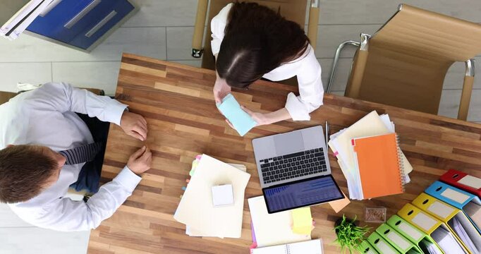 Man passes envelope containing bribe to woman across wooden desk in modern office setting. Businesswoman displeased and unwilling to accept money