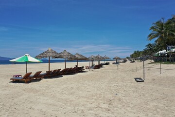 Sun umbrellas and beach chairs on tropical beach with palm trees. Summer vacation Vietnam