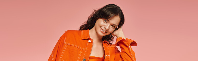 Stylish young woman radiates confidence in vibrant orange outfit against a pink backdrop