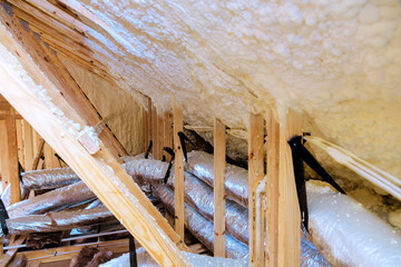 Workers are installing insulation in an attic, wooden beams ductwork for efficient heating cooling.