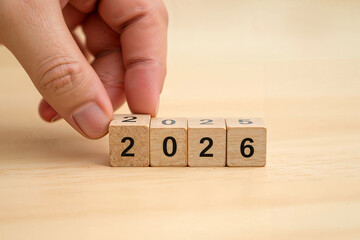 A hand moving wooden blocks with Loading bar between 2025 and 2026