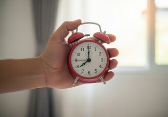 A hand holds a classic red alarm clock, symbolizing time, punctuality, and daily routine.