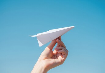 A hand launches a white paper airplane against a clear blue sky, symbolizing freedom and dreams.