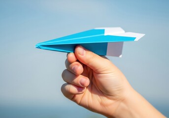 A hand launches a blue and white paper airplane against a clear blue sky, symbolizing freedom and dreams.