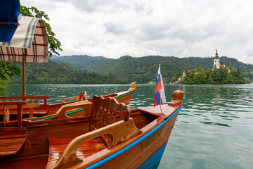 Two traditional wooden pletna boats are moored on the calm, green-blue waters of Lake Bled,...