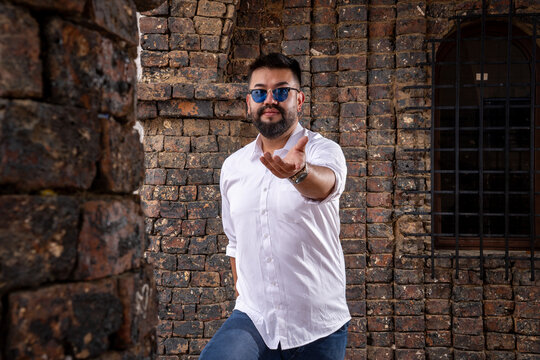 Bearded Latino man posing with attitude in a colonial castle structure in daylight. Fashion, modeling, tourism, and style concepts.