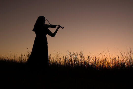 Silhouetted lady playing violin at sunset