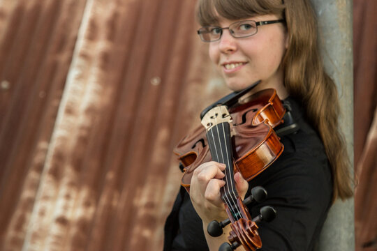 A girl holding her violin with rusty shed background