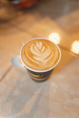 Latte with leaf foam art in paper cup on glossy surface