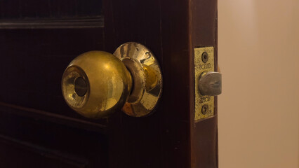 An aged brass doorknob on a dark wooden door, slightly ajar, showing wear and light reflections