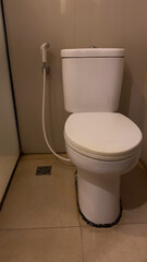 A white ceramic toilet with a closed lid stands in a bathroom, featuring a bidet spray next to it...