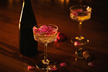 A bottle of champagne with delicate glasses and pink rose petals, creating an intimate and romantic ambiance.