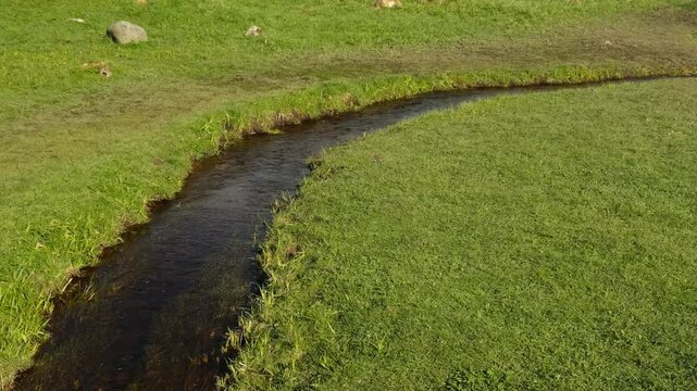 a narrow river between banks with green grass