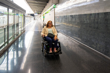 Smiling woman using electric wheelchair riding in subway station corridor. Concept of inclusion