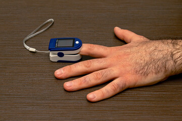 Male hand holding pulse oximeter on index finger measuring level of oxygen in blood