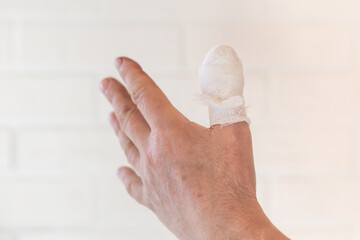 Bandaged left thumb against a light wall. Cuts, Injuries and First Aid