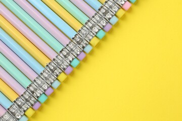 Many graphite pencils with erasers on yellow background, flat lay. Space for text