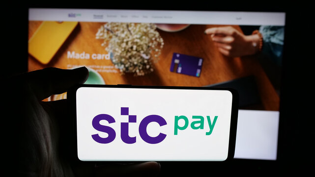Stuttgart, Germany - 06-13-2025: Person holding cellphone with logo of Saudi Arabian digital secure wallet STC Pay on screen in front of webpage. Focus on phone display.
