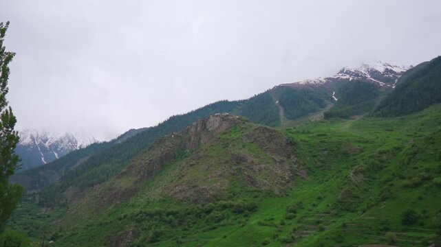 Handheld shot of Triloknath village on side of a cliffside mountain as seen from the road towards Udaipur in Pattan valley, Himachal Pradesh, India. Scenic view of village in the Himalayas.