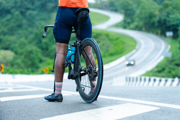A cyclist wearing colorful socks and an orange jersey pauses with their bike on a wet road near a...