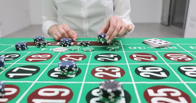 Woman carefully places casino chips on green roulette table with numerous numbers and betting grids. Focus on action of playing table game slow motion