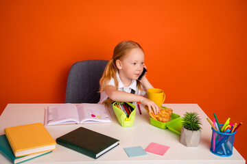 Young girl multitasking at desk with books, snacks, and colorful materials, seated against bright...