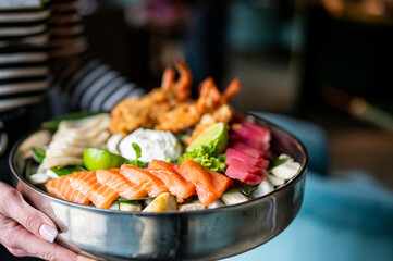 Close-up of assorted fresh seafood in a bowl, including salmon, tuna, shrimp, and squid, garnished with greens, lime, and sauce. Colorful, appetizing, and ideal for food themes.