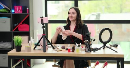 Happy beauty blogger puts on headband with cat ears recording video at home. Smiling woman shoots tutorial of cosmetics usage using smartphone at desk - Powered by Adobe
