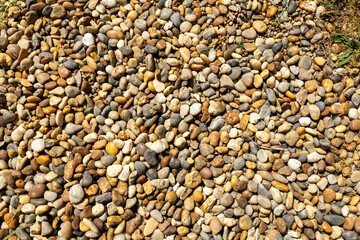 Top view of a collection of smooth, multicolored river pebbles lying on the ground. 