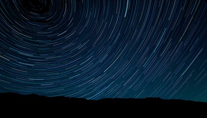 Star trails across a dark night sky, creating swirling patterns above a silhouette of distant mountains.