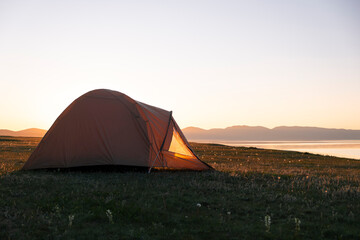 Sunset landscape with SUV car and set up tent at camping site by highland freshwater lake surrounded by high mountains. Song Kul Lake, Kyrgyzstan, Central Asia. Road trip, travel camping concept.