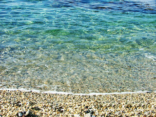 A beautiful pebble beach along the Calabrian coast in southern Italy, where smooth stones in natural tones stretch along the shoreline. The crystal-clear turquoise waters of the Tyrrhenian Sea.