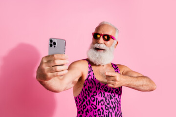 Photo of positive nice senior man wear swimwear shooting streaming blogging isolated on pink color background © deagreez