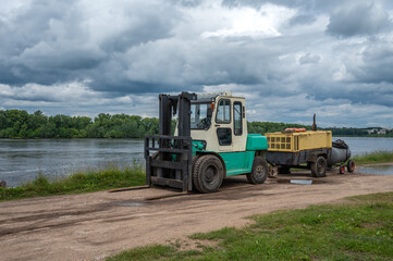 A forklift with a compressor on a trailer on the river bank.