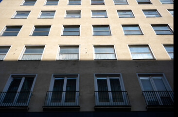Minimalist urban building facade with repetitive windows in soft light and shadow. Simple design with clear geometry and soft beige tones creates a modern aesthetic for city environments.

