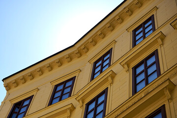 Yellow historic building facade with wooden framed windows under clear blue sky. Classic architecture detail highlights symmetry and elegance of old urban design.