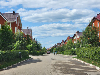A street in a cottage village with red brick houses surrounded by lush greenery on a sunny summer...