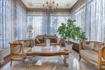 A glazed terrace in a country house with elegant classical furniture. The panoramic windows are decorated with beautiful tulle.