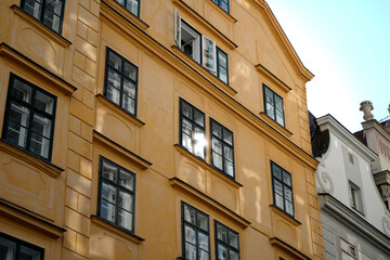 Yellow urban facade with rhythmic windows and one open shutter. Glass reflects daylight softly. Elegant symmetry and warm color highlight traditional European style.

