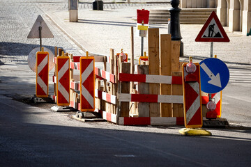 Street construction site with wooden barriers and traffic signs. Red and white stripes indicate...